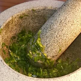 Un mortier rempli de tiges d'ail des ours, menant au livret "Je cuisine l'ail des ours" de L'Aventure au coin du bois, présentant des recettes printanières sans gluten à base de cette plante des sous-bois.